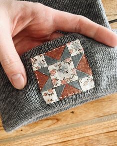 a hand is holding a patch on top of a gray sweater that has a flower pattern