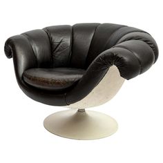 a black and white leather chair sitting on top of a white pedestal with an oval foot rest