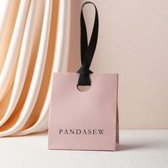 a pink paper bag with a black ribbon hanging from it's side on a white surface