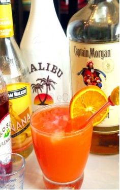 a close up of an orange drink in a glass near bottles and glasses on a table