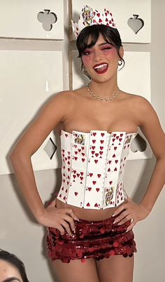 a woman wearing a white corset and red sequin skirt with hearts on it