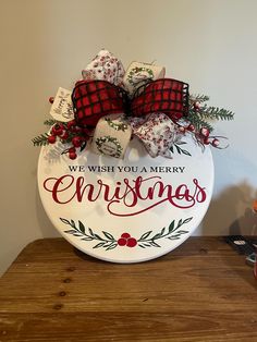 we wish you a merry christmas sign with red bows and plaid bow on it sitting on a wooden table