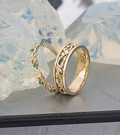 two gold wedding rings with green stones sitting on top of a table next to crystal rocks