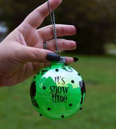 a hand holding a green ornament with it's snow time written on it