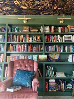 a pink chair sitting in front of a book shelf filled with books