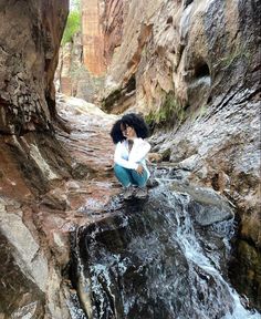 a woman sitting on top of a rock next to a river in a canyon filled with rocks