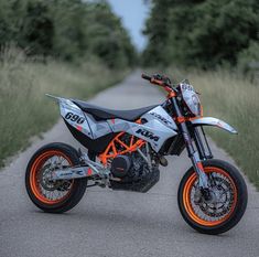 an orange and white motorcycle parked on the side of a road next to tall grass