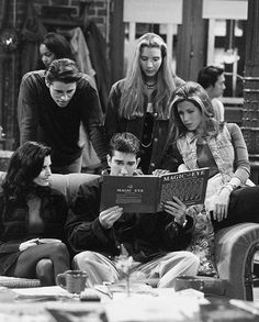 black and white photograph of four people sitting on a couch looking at an open book