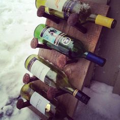 several bottles of wine are lined up on a wooden rack in the snow, with one bottle left open