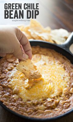 a hand dipping a tortilla chip into a skillet filled with green chile bean dip