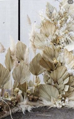 an arrangement of dried flowers and plants in front of a white wall