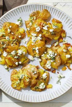 a white plate topped with potatoes covered in feta cheese on top of a wooden table