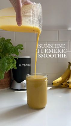 a person pouring orange juice into a glass on top of a counter next to bananas