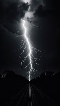 a black and white photo of a lightning bolt in the sky over a train track