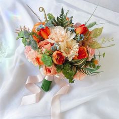 a bridal bouquet with orange and pink flowers on a white cloth covered bed sheet