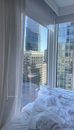 an unmade bed sitting in front of a window next to a tall building with lots of windows