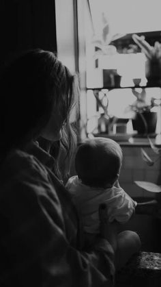 a woman holding a baby in her arms while looking out the window at something outside