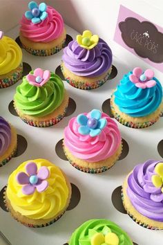 cupcakes decorated with colorful frosting and flowers in a white box on a table