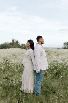 a pregnant couple standing in the middle of a field