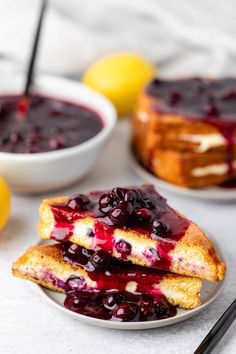 two slices of french toast with blueberry sauce and lemon wedges on the side