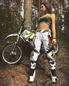 a woman standing next to a dirt bike in the woods