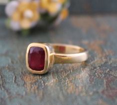 a gold ring with a red stone in the middle on a table next to flowers