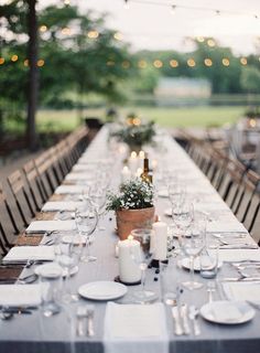 a long table is set with white plates and silverware for an outdoor dinner party