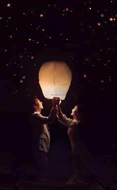 two people holding up a paper lantern in the dark