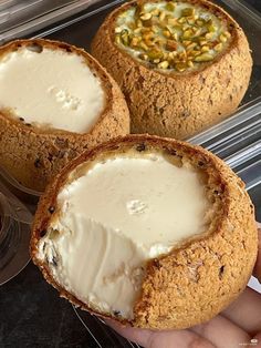 three baked desserts in plastic containers with toppings on them and one being held by someone's hand