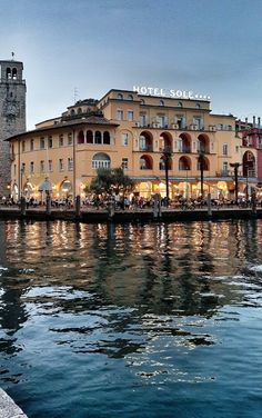 an old building is next to the water in front of a clock tower at dusk