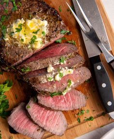 sliced steak with butter and parsley on cutting board next to knife, fork and pepper shaker