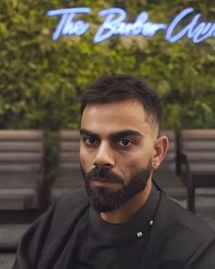 a man with a beard and black shirt sitting in front of a wall that says the better club