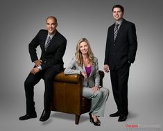 two men and a woman in business attire posing for a photo on a gray background