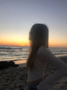 a woman standing on top of a sandy beach next to the ocean at sun set