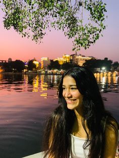 a woman sitting on top of a boat in the water at sunset with buildings in the background