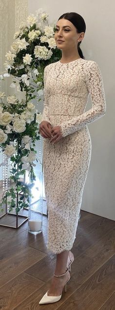 a woman standing in front of a vase with white flowers and wearing a long sleeved dress