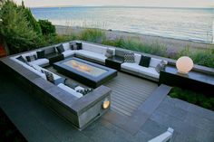 an outdoor living area with couches, tables and fire pit in front of the ocean