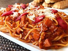 a plate of spaghetti with meat and cheese on it, next to some breadsticks