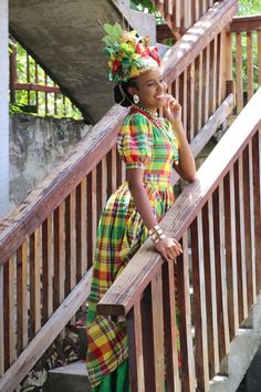 a woman in a colorful dress leaning on a wooden railing and talking on a cell phone