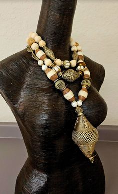 Three strands of exotic, wild and rare beads adorn this tribal - ethnic inspired Tibetan, Asian and African oversized beaded chest piece, which either men or women can wear. A very large (4" x 2.5") hand crafted African lost wax brass crocodile bead is the pendant on this bold piece. The other components include magnesite, Chinese vintage brass coins, gold aurora borealis rhinestone rondelles, African bone and wood bicone beads, more lost wax brass cagework beads, Tibetan brass repousse, brass cagework conch beads, round blonde wood beads, beige wood barrel beads, African brass sundials and small bone rondelles. Despite it's size, this is a fairly lightweight piece with only the pendant bead having any real weight. Adjusts from 17-20". Gold tone hardware, a lobster claw clasp and a 3" exte Bohemian Beaded Necklace With Large Beige Beads, Traditional Beaded Beige Jewelry, Bohemian Beige Beaded Necklace With Large Beads, Bohemian Beige Beads For Beach, Beige Bohemian Beads For Beach, Bohemian Beige Beach Beads, Traditional Ceremonial Necklace With Large Beads, Vintage Ceremonial Necklace With Large Beads, Luxury Large Bead Amulet Jewelry