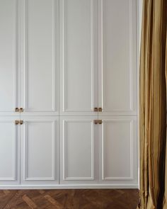 a white closet with gold handles and doors in a room that has wooden floors, wood flooring, and beige drapes