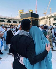 two people hugging each other in front of a building with many others standing around it