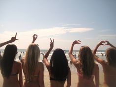 four girls standing on the beach with their hands in the air and making heart signs