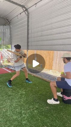 two men are practicing baseball batting in the batting cage with one man holding a catcher's mitt