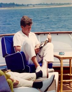 a man sitting on a blue chair in front of the ocean with his feet up