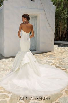 a woman in a white wedding dress standing on a stone walkway with her back turned to the camera