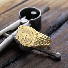 Discover our exquisite solid gold signet ring, crafted in 10k, 14k, or 18k yellow gold, and inspired by the timeless mythology of the Norse. At the center of the design, Yggdrasil, the sacred Tree of Life, is masterfully engraved, representing the connection of all things in the cosmos. Surrounding the tree are ancient Norse runes, adding depth and mystery to the piece. The sides of the ring are decorated with intricate Norse braid patterns, enhancing its historical allure. This unique signet ring combines traditional symbolism with luxurious craftsmanship, making it a powerful and meaningful statement piece. This ring also comes with a high quality gift box with a message engraved on the top. You can write what you would like engraved in the notes section when checking out. - Material: So Norse Braid, Nordic Warrior, Warrior Ring, Sacred Tree, Norse Runes, Braid Patterns, Norse Vikings, Gold Signet Ring, Custom Ring