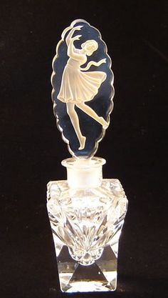 a small glass bottle with a figure on it's top and an object in the shape of a ballerina