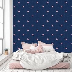 a bed with pink hearts on it in front of a dark blue wall and window