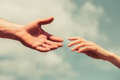 two hands reaching out towards each other in the air against a blue sky with white clouds